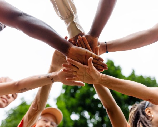 Directly below shot of multiracial volunteers stacking hands during environmental cleanup program. Multiethnic men and women cheering before cleaning the city park.